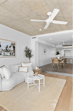 Modern living room with white sofa, ceiling fan, and open-plan dining area.