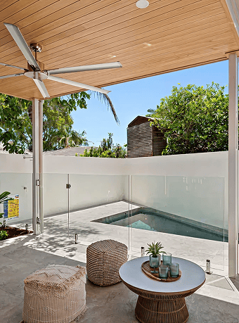 Outdoor patio with pool, ceiling fan, and lush greenery in the background.