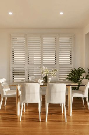 Modern dining room with white shutters and a wooden table with six chairs.