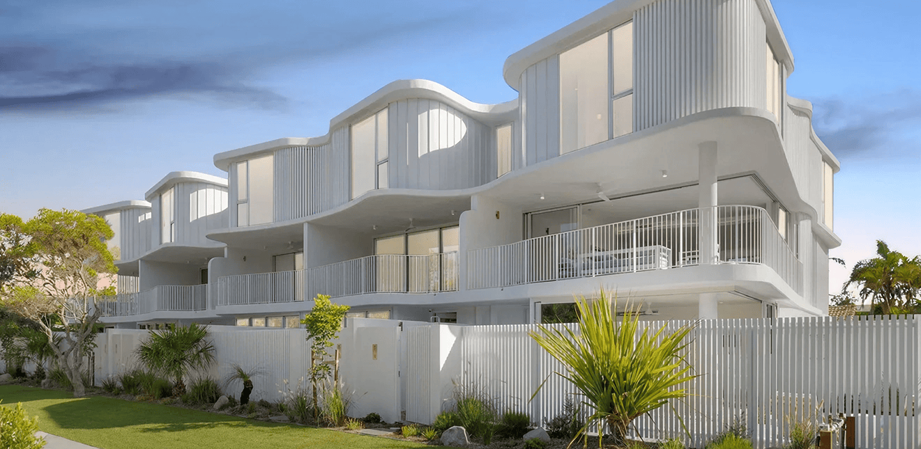 Modern white beachfront apartment building with curved balconies and lush landscaping.